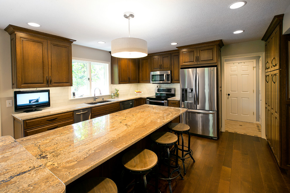 Eat-in kitchen - transitional l-shaped medium tone wood floor eat-in kitchen idea with a double-bowl sink, raised-panel cabinets, dark wood cabinets, granite countertops, white backsplash, glass tile backsplash, stainless steel appliances and an island