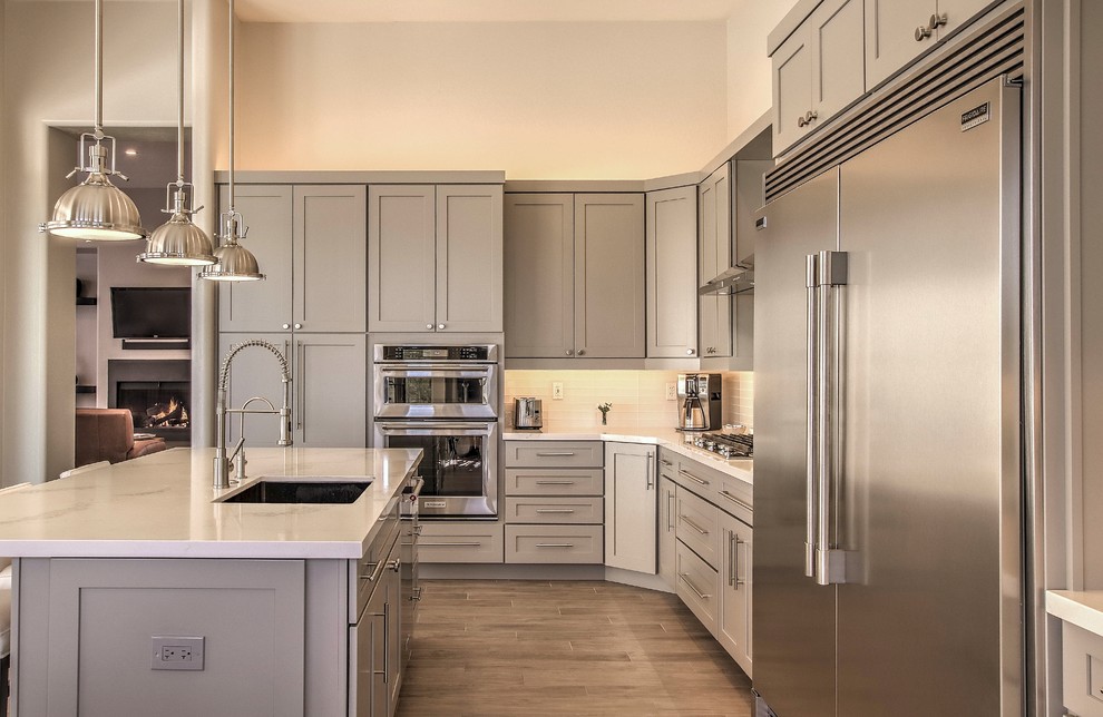 Example of a large transitional l-shaped porcelain tile and brown floor eat-in kitchen design in Phoenix with a single-bowl sink, shaker cabinets, gray cabinets, quartz countertops, white backsplash, glass tile backsplash, stainless steel appliances, an island and white countertops