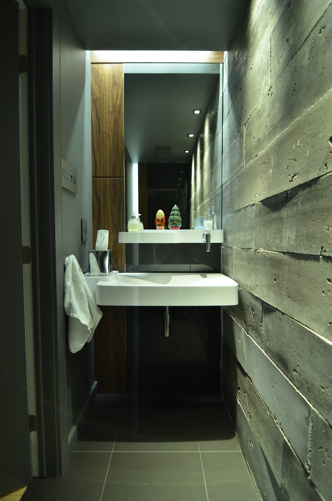 This is an example of a small industrial powder room in Montreal with dark wood cabinets, porcelain tile, grey walls, porcelain floors, a wall-mount sink and gray tile.