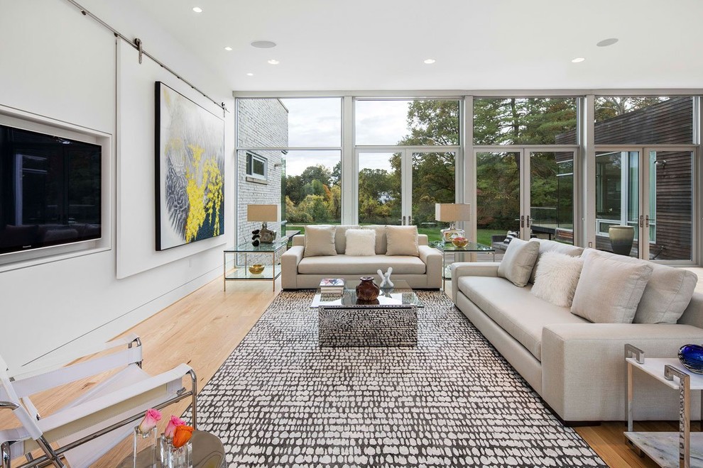 This is an example of a large contemporary open concept living room in St Louis with white walls, light hardwood floors, no fireplace and a concealed tv.