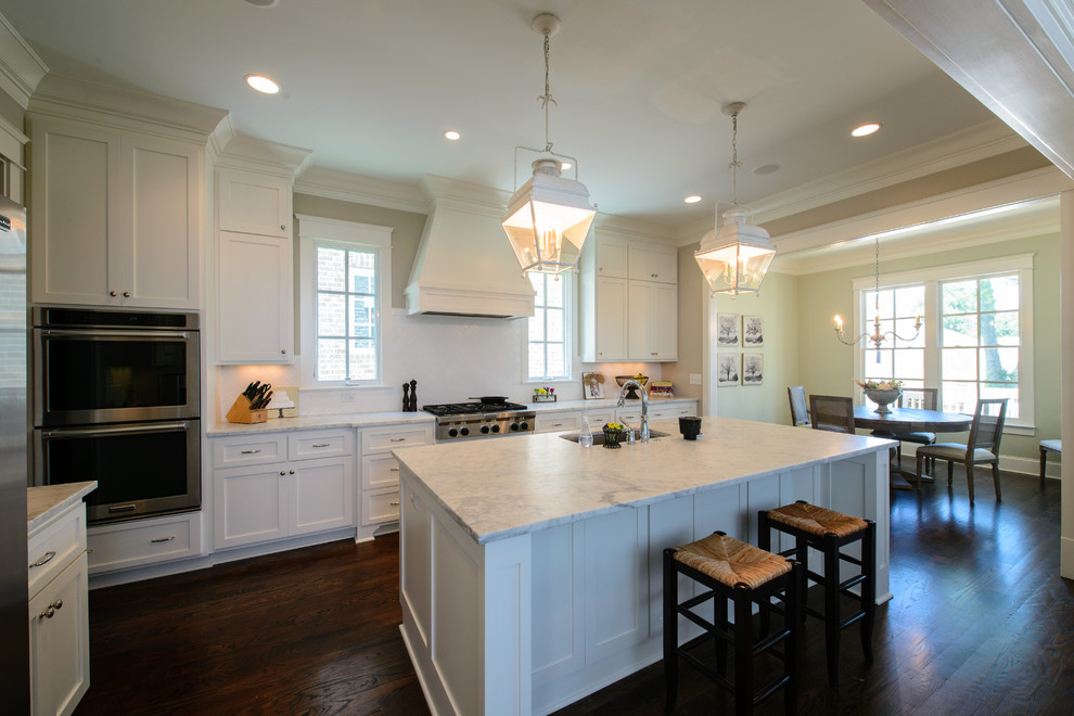 Design ideas for a mid-sized traditional l-shaped eat-in kitchen in Nashville with an undermount sink, recessed-panel cabinets, white cabinets, marble benchtops, white splashback, ceramic splashback, stainless steel appliances, medium hardwood floors and with island.