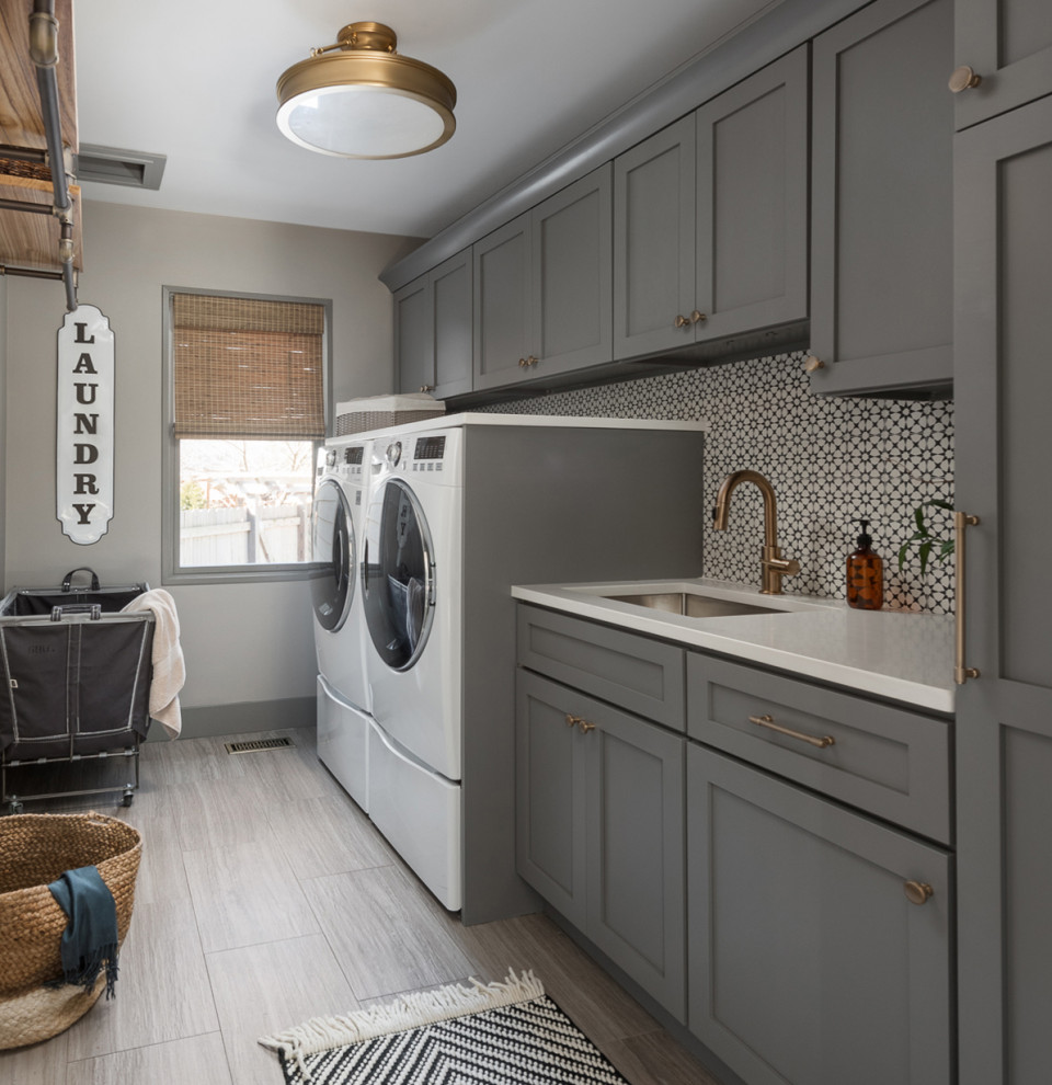 Mid-sized transitional single-wall dedicated laundry room in Chicago with an undermount sink, shaker cabinets, grey cabinets, quartz benchtops, multi-coloured splashback, cement tile splashback, grey walls, porcelain floors, a side-by-side washer and dryer, grey floor and white benchtop.