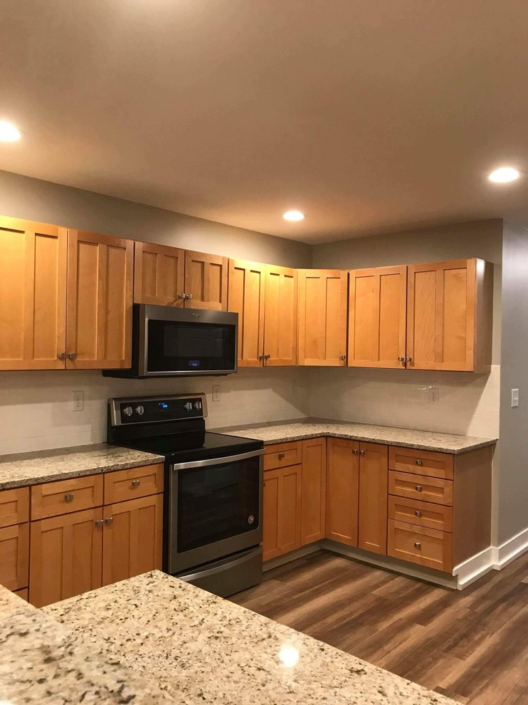 This is an example of a mid-sized traditional u-shaped separate kitchen in Grand Rapids with a double-bowl sink, shaker cabinets, light wood cabinets, granite benchtops, white splashback, subway tile splashback, stainless steel appliances, medium hardwood floors and brown floor.