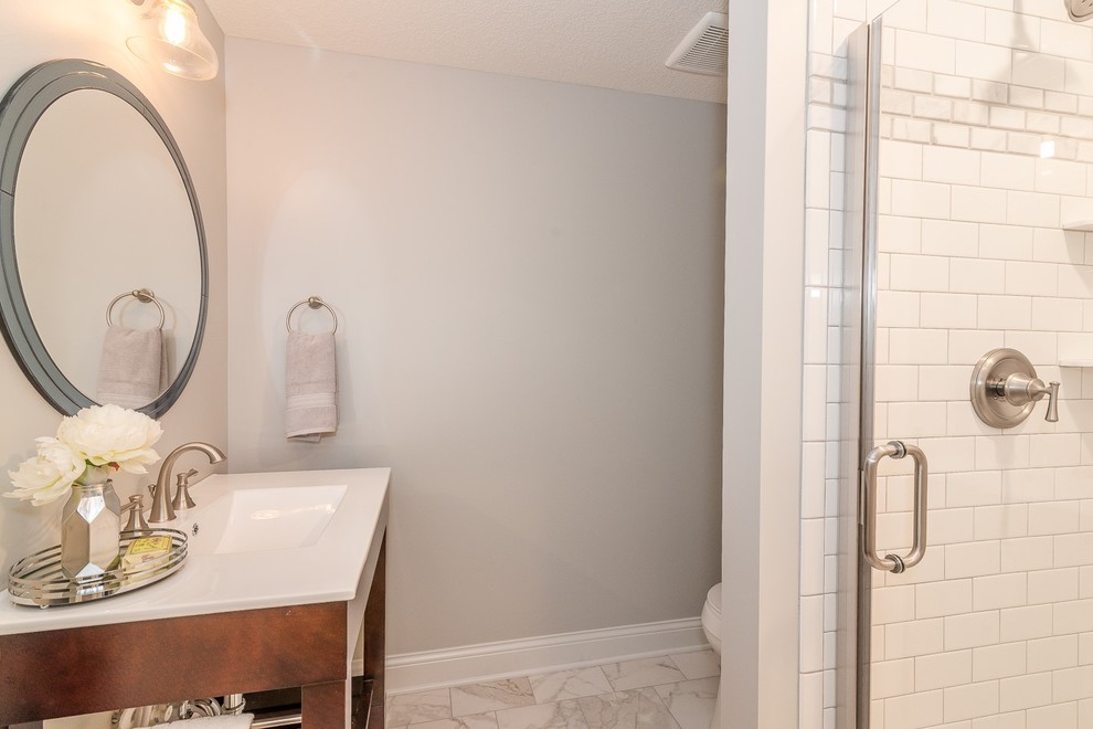 Design ideas for a small transitional 3/4 bathroom in Minneapolis with furniture-like cabinets, medium wood cabinets, a corner shower, white tile, subway tile, grey walls, marble floors, an integrated sink, engineered quartz benchtops, white floor, a hinged shower door and white benchtops.