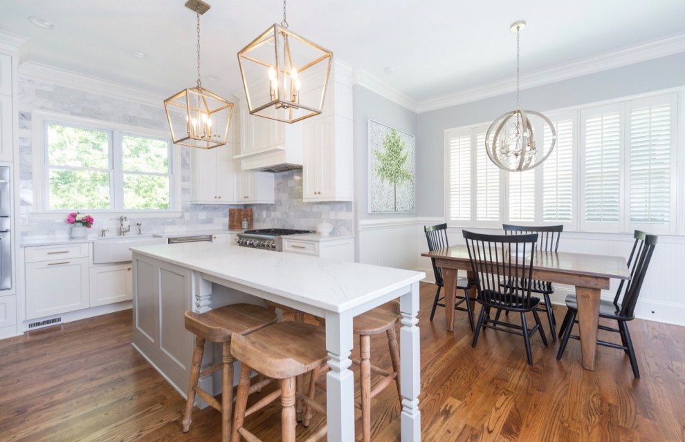 Photo of a large transitional u-shaped eat-in kitchen in Charlotte with a farmhouse sink, shaker cabinets, white cabinets, quartzite benchtops, white splashback, marble splashback, stainless steel appliances, light hardwood floors, with island, brown floor and white benchtop.