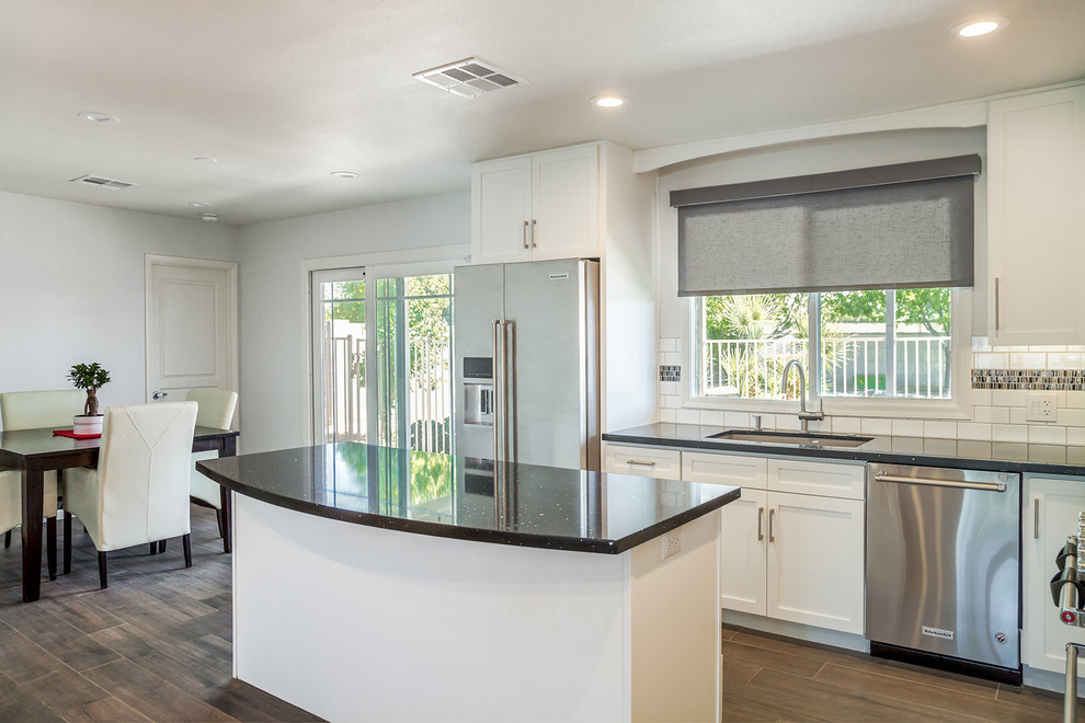 Inspiration for a large transitional l-shaped porcelain tile and brown floor eat-in kitchen remodel in Phoenix with an undermount sink, recessed-panel cabinets, white cabinets, quartz countertops, black backsplash, ceramic backsplash, stainless steel appliances and an island