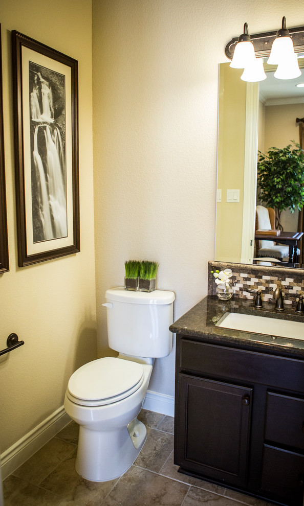 Design ideas for a mid-sized traditional powder room in Austin with shaker cabinets, a two-piece toilet, beige walls, travertine floors, an undermount sink, granite benchtops and dark wood cabinets.