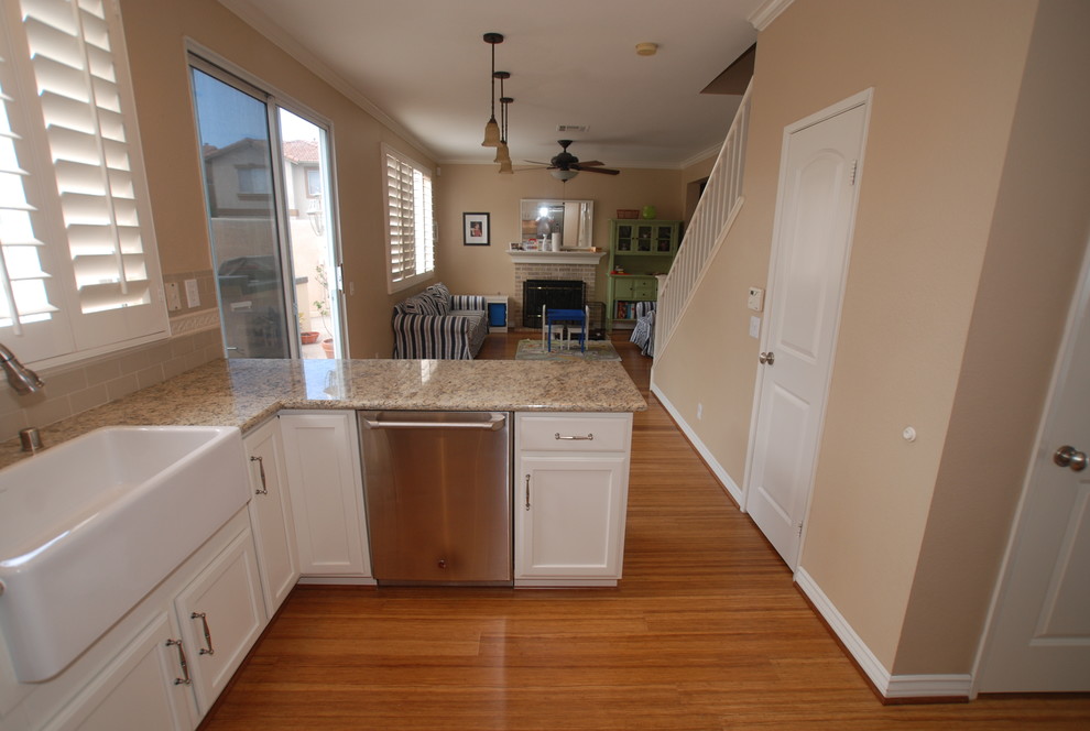 Small traditional u-shaped open plan kitchen in Orange County with a farmhouse sink, recessed-panel cabinets, white cabinets, granite benchtops, beige splashback, subway tile splashback, stainless steel appliances, bamboo floors and a peninsula.