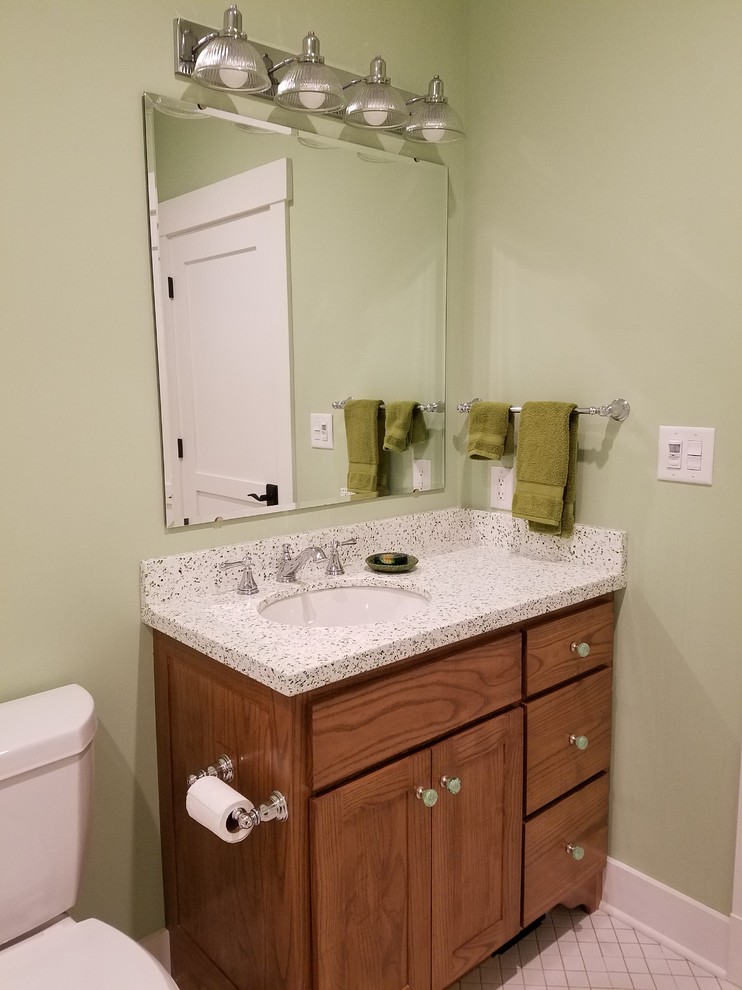 This is an example of a mid-sized transitional powder room in Other with furniture-like cabinets, medium wood cabinets, a two-piece toilet, white tile, ceramic tile, green walls, mosaic tile floors, an undermount sink, terrazzo benchtops and beige floor.