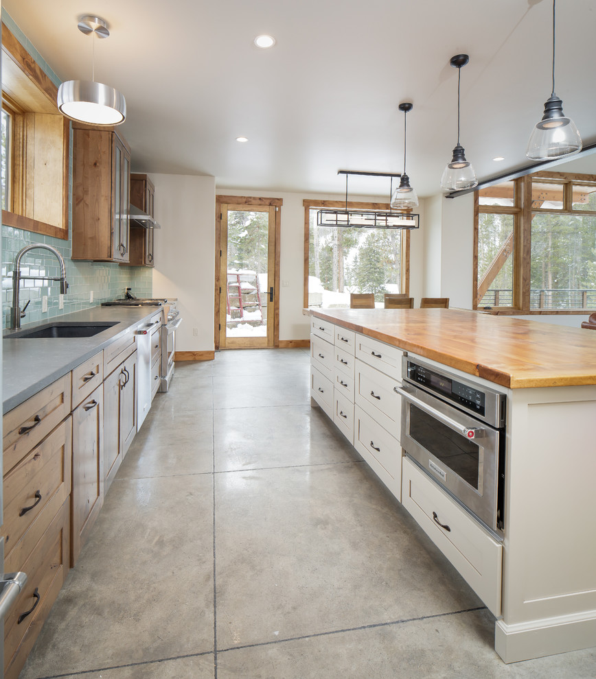 Example of a mid-sized mountain style single-wall eat-in kitchen design in Denver with an undermount sink, shaker cabinets, distressed cabinets, quartz countertops, blue backsplash, glass tile backsplash, stainless steel appliances, an island and gray countertops