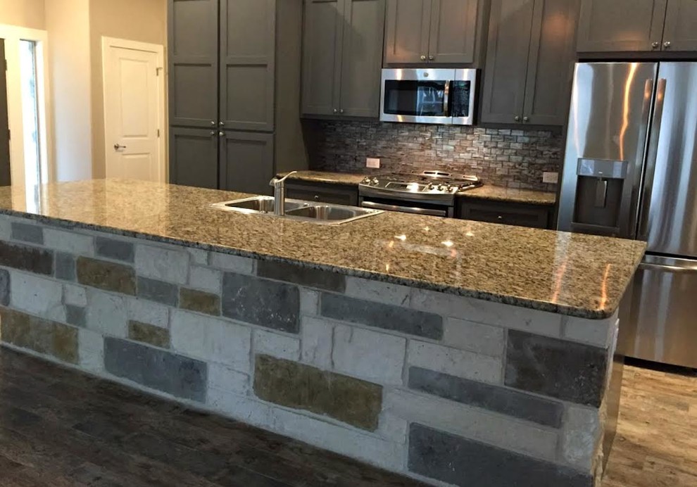 Open concept kitchen - mid-sized transitional galley medium tone wood floor and brown floor open concept kitchen idea in Austin with a double-bowl sink, shaker cabinets, gray cabinets, granite countertops, gray backsplash, glass tile backsplash, stainless steel appliances and an island