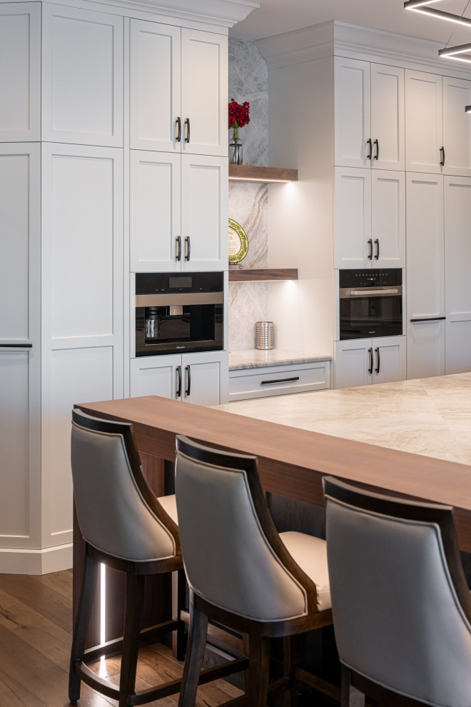 Example of a large transitional medium tone wood floor and brown floor open concept kitchen design with a double-bowl sink, flat-panel cabinets, white cabinets, quartzite countertops, beige backsplash, stainless steel appliances, an island and beige countertops