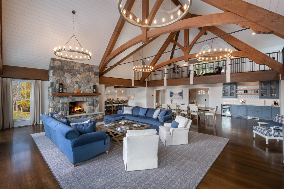 Photo of an expansive classic open plan games room in Bridgeport with white walls, dark hardwood flooring, a standard fireplace, a stone fireplace surround, a wall mounted tv, brown floors and exposed beams.