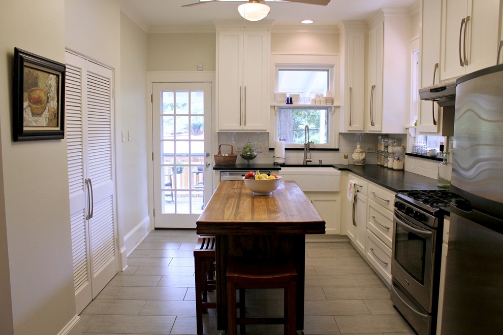 Photo of a small country l-shaped separate kitchen in New Orleans with a farmhouse sink, shaker cabinets, white cabinets, soapstone benchtops, white splashback, subway tile splashback, stainless steel appliances, ceramic floors, with island and grey floor.