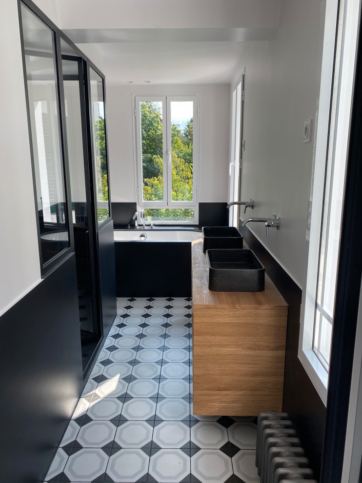 Alcove shower - small modern 3/4 black tile ceramic tile and double-sink alcove shower idea in Paris with glass-front cabinets, light wood cabinets, an undermount tub, a wall-mount toilet, a drop-in sink, wood countertops, a hinged shower door and a floating vanity