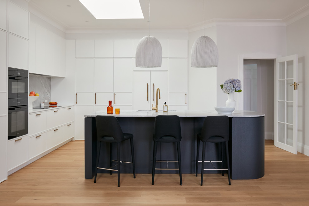 Idéer för att renovera ett mellanstort funkis vit vitt kök med öppen planlösning, med en enkel diskho, skåp i shakerstil, vita skåp, marmorbänkskiva, vitt stänkskydd, stänkskydd i marmor, svarta vitvaror, ljust trägolv, en köksö och brunt golv