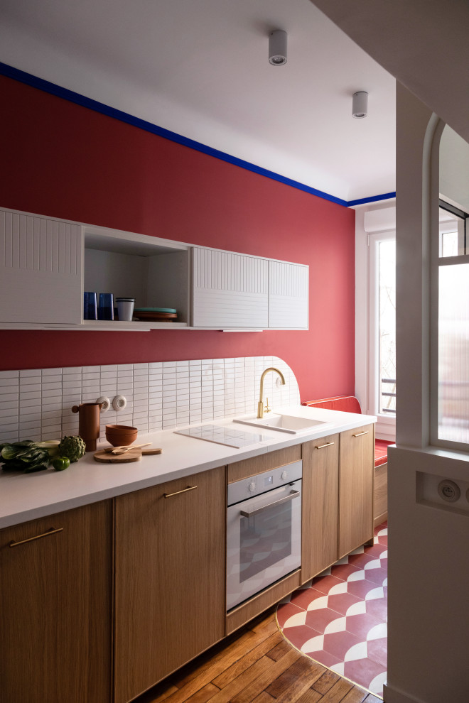 Idée de décoration pour une petite cuisine américaine linéaire minimaliste en bois clair avec un évier 1 bac, un placard à porte affleurante, un plan de travail en stratifié, une crédence blanche, une crédence en mosaïque, un électroménager blanc, carreaux de ciment au sol, un sol rouge et un plan de travail blanc.