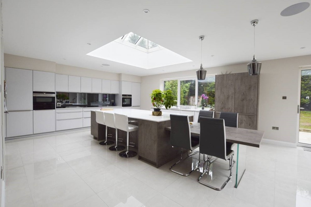 This is an example of a large contemporary l-shaped open plan kitchen in Other with an integrated sink, flat-panel cabinets, grey cabinets, metallic splashback, mirror splashback, stainless steel appliances, porcelain floors, multiple islands, white floor, white benchtop and coffered.