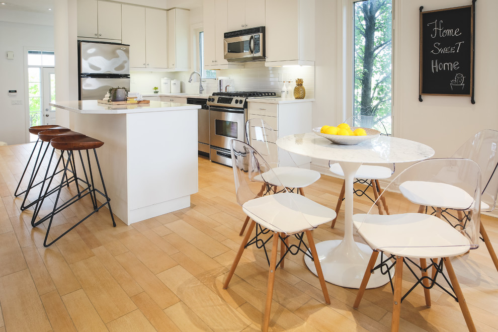 Photo of a small scandinavian l-shaped eat-in kitchen in Toronto with an undermount sink, flat-panel cabinets, white cabinets, quartz benchtops, white splashback, subway tile splashback, stainless steel appliances, porcelain floors, with island and white benchtop.