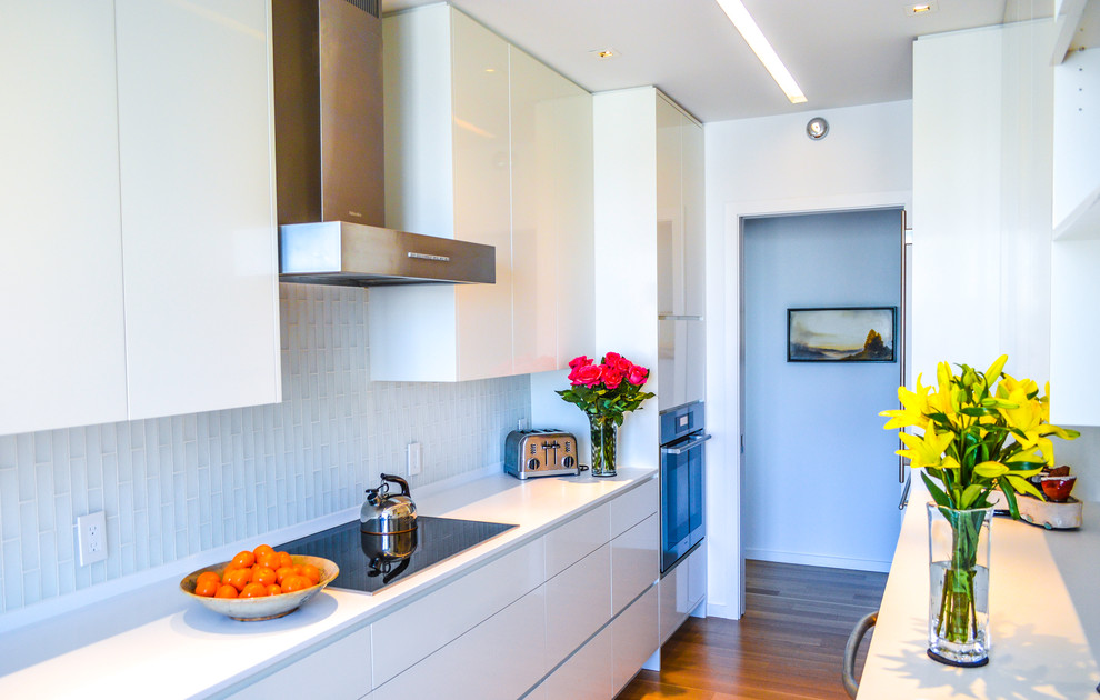 This is an example of a small modern galley separate kitchen in Atlanta with an undermount sink, flat-panel cabinets, white cabinets, solid surface benchtops, white splashback, glass tile splashback, stainless steel appliances, light hardwood floors and no island.