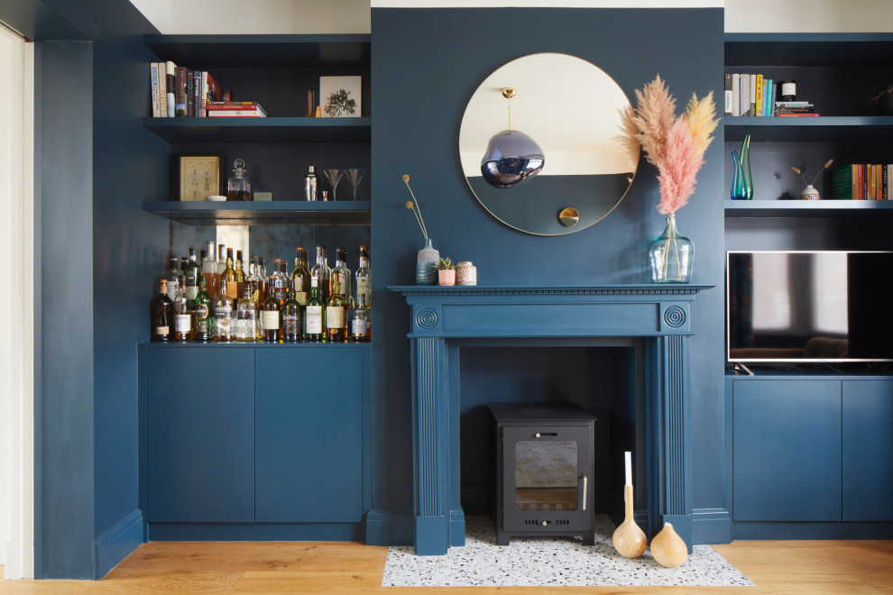 Offenes, Mittelgroßes Modernes Wohnzimmer mit braunem Holzboden, blauer Wandfarbe, Kamin, Kaminumrandung aus Holz und freistehendem TV in London