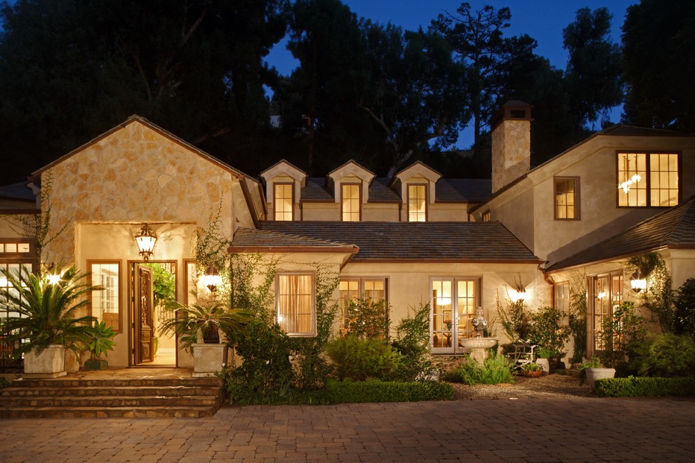 Photo of an expansive country two-storey beige exterior in Los Angeles with stone veneer and a gable roof.