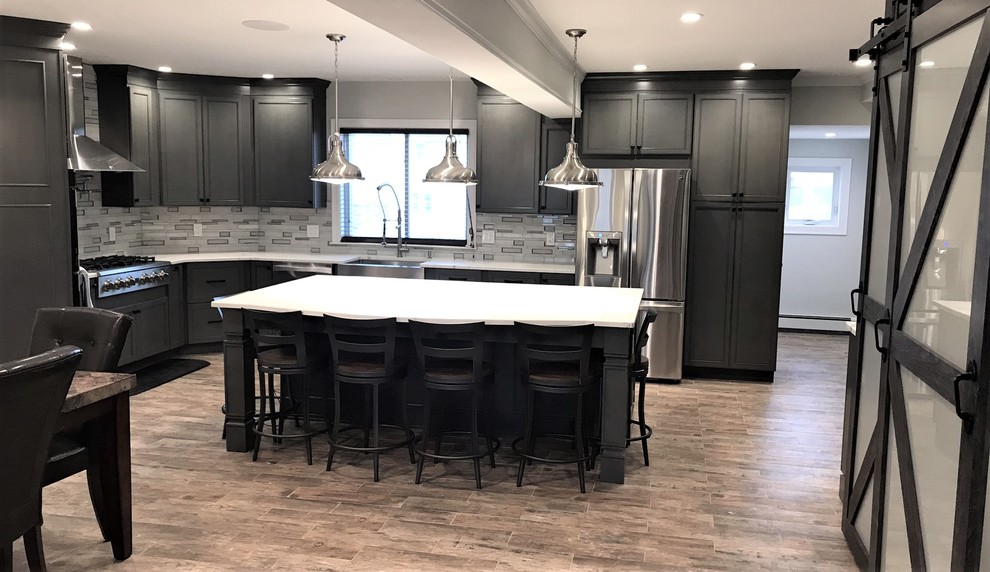 Large transitional l-shaped eat-in kitchen in Boston with a farmhouse sink, shaker cabinets, grey cabinets, quartz benchtops, metallic splashback, glass tile splashback, stainless steel appliances, porcelain floors, with island and brown floor.