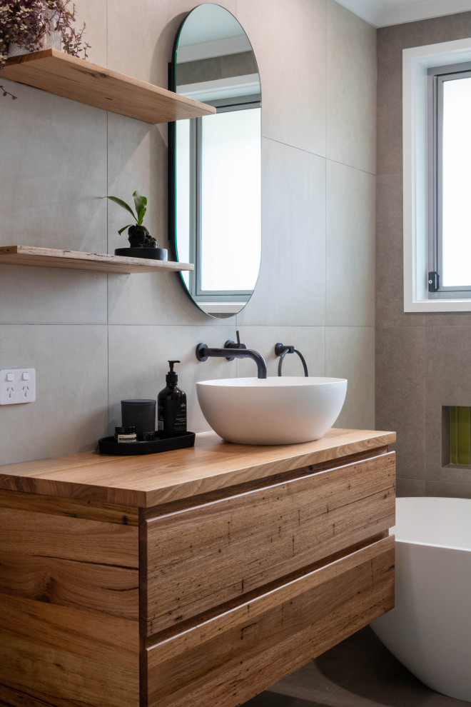 Cette photo montre une salle de bain tendance en bois brun avec un placard à porte plane, une baignoire indépendante, un carrelage gris, un lavabo encastré, un plan de toilette en bois, un sol gris, un plan de toilette marron, meuble simple vasque et meuble-lavabo suspendu.
