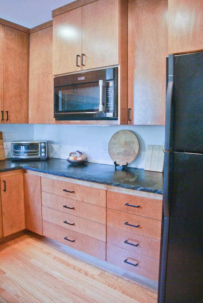 Small contemporary u-shaped eat-in kitchen in Sacramento with a drop-in sink, flat-panel cabinets, medium wood cabinets, soapstone benchtops, black appliances, medium hardwood floors and a peninsula.