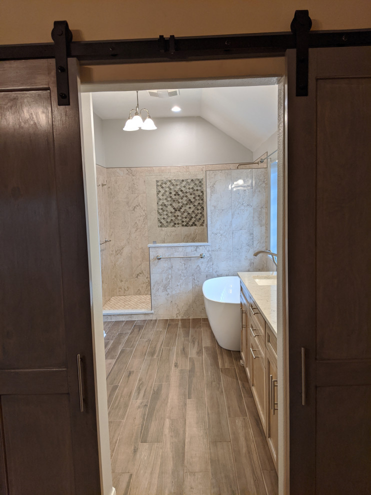 Design ideas for a mid-sized traditional master bathroom in Houston with shaker cabinets, medium wood cabinets, a freestanding tub, an open shower, a one-piece toilet, beige tile, marble, grey walls, wood-look tile, an undermount sink, engineered quartz benchtops, brown floor, an open shower, beige benchtops, a shower seat, a double vanity and a built-in vanity.