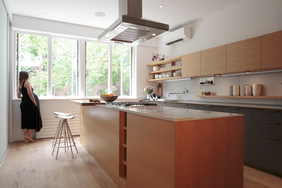 This is an example of a mid-sized modern galley open plan kitchen in New York with flat-panel cabinets, light wood cabinets, quartzite benchtops, white splashback, with island, an undermount sink, stone slab splashback, stainless steel appliances, light hardwood floors and beige floor.
