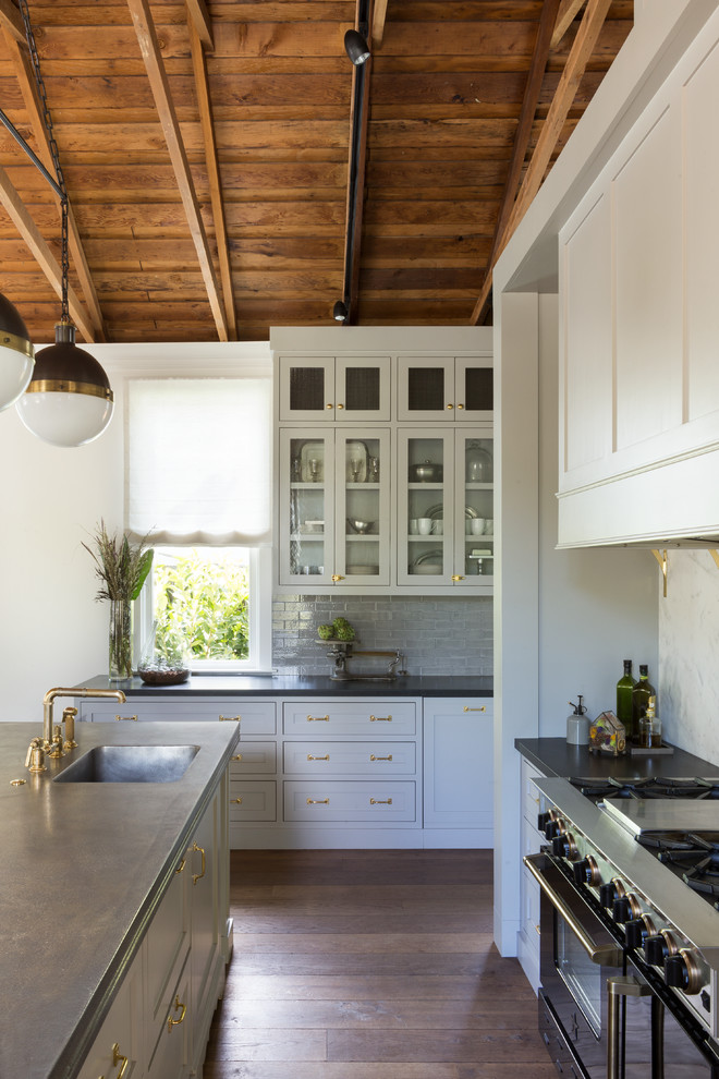 Design ideas for a transitional u-shaped open plan kitchen in San Francisco with an undermount sink, glass-front cabinets, white cabinets, grey splashback, ceramic splashback, medium hardwood floors, multiple islands and stainless steel appliances.