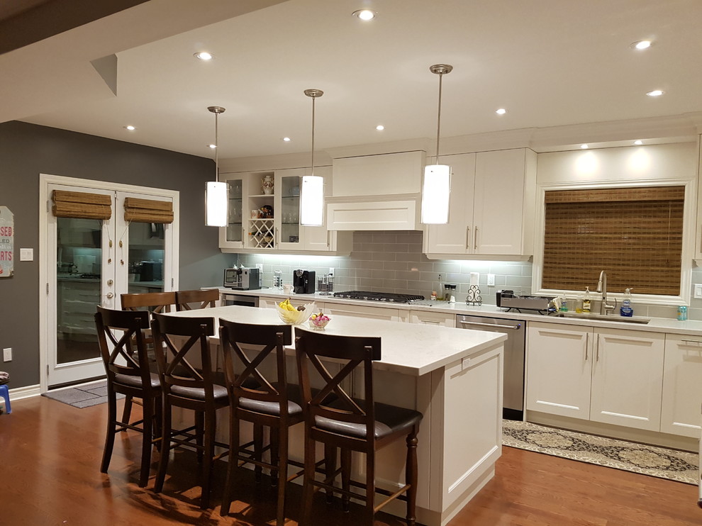 Example of a large transitional l-shaped dark wood floor and brown floor open concept kitchen design in Toronto with an undermount sink, shaker cabinets, white cabinets, quartz countertops, gray backsplash, subway tile backsplash, stainless steel appliances and an island