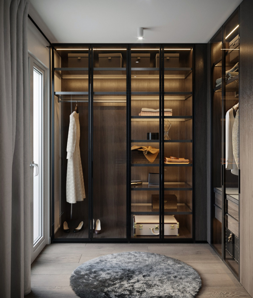 This is an example of a mid-sized contemporary gender-neutral walk-in wardrobe in Other with glass-front cabinets, black cabinets, medium hardwood floors and beige floor.