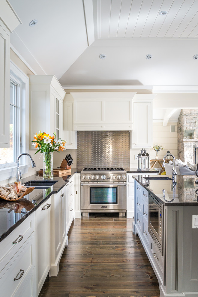 Beach style u-shaped kitchen in Toronto with a double-bowl sink, recessed-panel cabinets, white cabinets, metallic splashback, matchstick tile splashback, stainless steel appliances, dark hardwood floors, with island and brown floor.