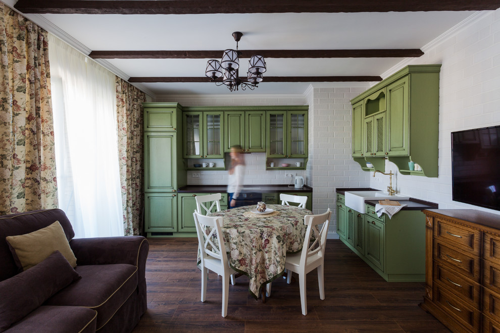 This is an example of a small country l-shaped open plan kitchen in Saint Petersburg with a farmhouse sink, recessed-panel cabinets, green cabinets, laminate benchtops, white splashback, ceramic splashback, black appliances, laminate floors, no island, brown floor and brown benchtop.