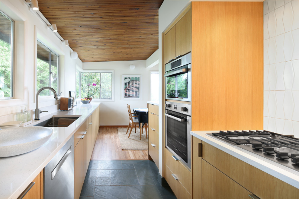 Mid-sized midcentury galley eat-in kitchen in Seattle with an undermount sink, flat-panel cabinets, quartz benchtops, white splashback, stainless steel appliances, slate floors, no island, grey floor, white benchtop and medium wood cabinets.