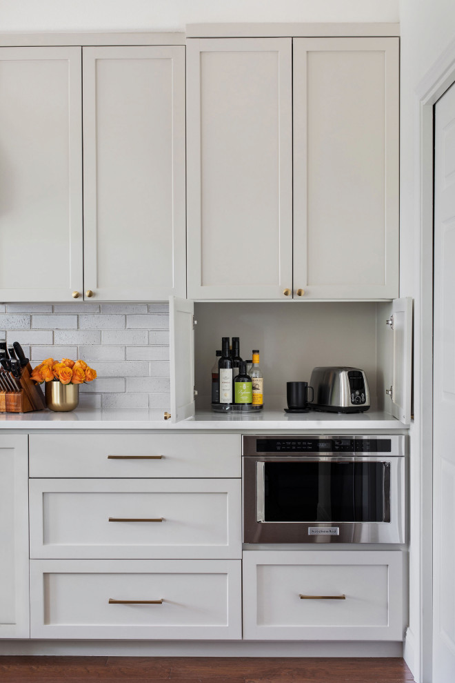 Example of a mid-sized transitional medium tone wood floor and brown floor open concept kitchen design in Austin with an undermount sink, shaker cabinets, gray cabinets, quartz countertops, white backsplash, brick backsplash, stainless steel appliances, a peninsula and white countertops
