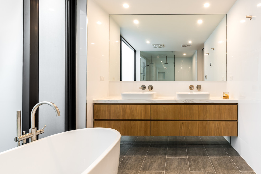 Photo of a mid-sized contemporary master bathroom in Adelaide with flat-panel cabinets, light wood cabinets, a freestanding tub, a double shower, a one-piece toilet, white tile, cement tile, white walls, ceramic floors, a vessel sink, marble benchtops, grey floor, an open shower and white benchtops.