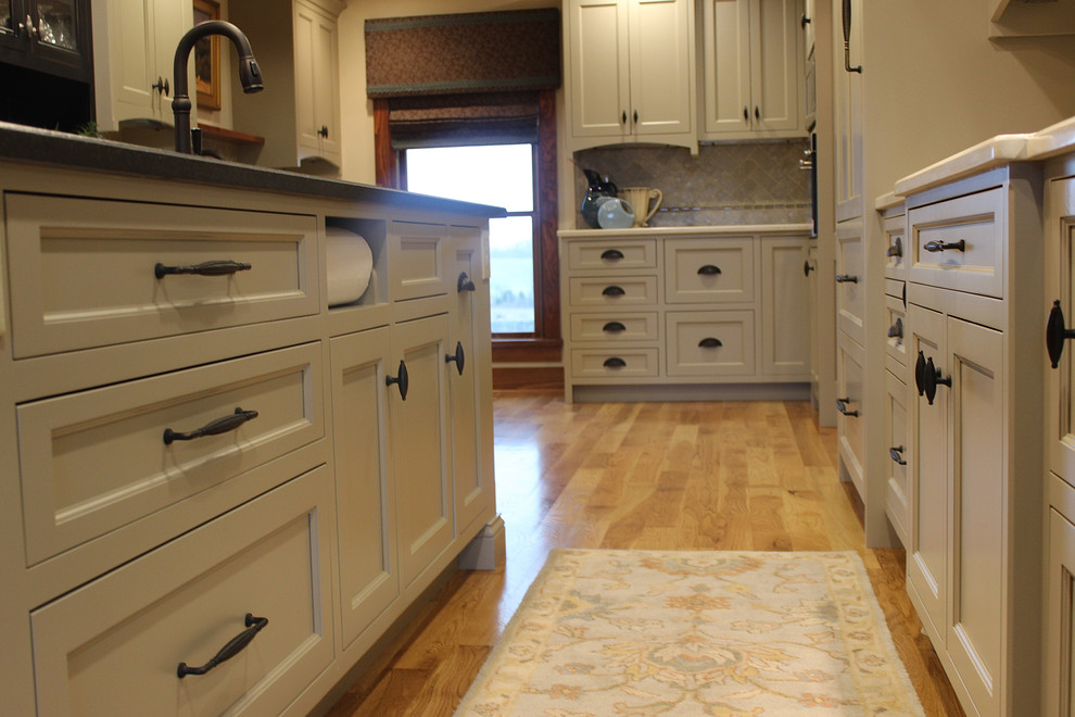 Mid-sized mountain style u-shaped medium tone wood floor eat-in kitchen photo with an undermount sink, shaker cabinets, white cabinets, solid surface countertops, brown backsplash, ceramic backsplash, stainless steel appliances and an island