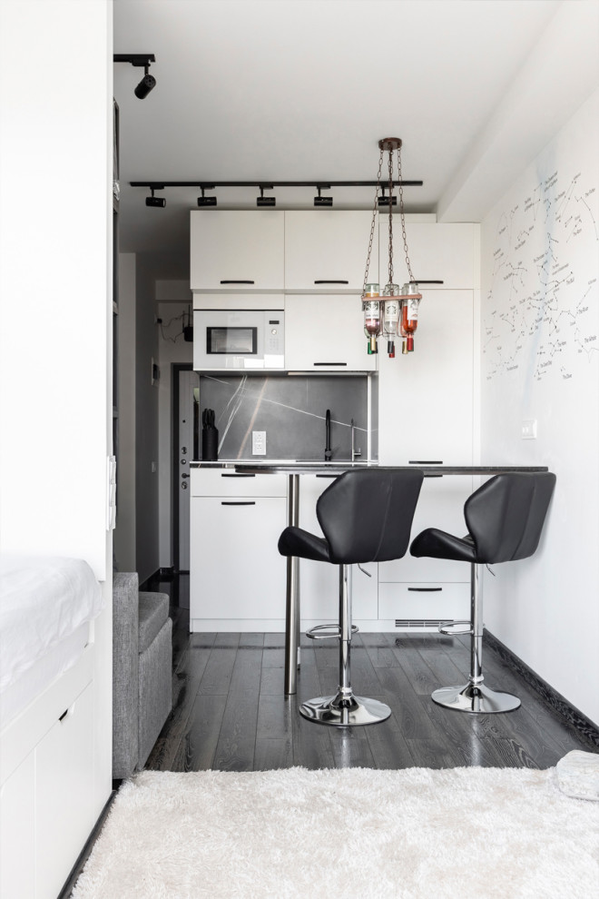 Small contemporary single-wall open plan kitchen in Moscow with an undermount sink, flat-panel cabinets, white cabinets, tile benchtops, black splashback, porcelain splashback, white appliances, painted wood floors, no island, black floor and black benchtop.