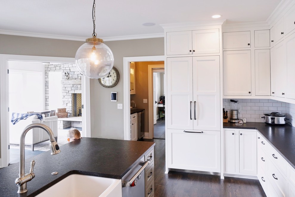 Example of a mid-sized transitional l-shaped dark wood floor and brown floor eat-in kitchen design in Minneapolis with a farmhouse sink, white backsplash, porcelain backsplash, stainless steel appliances, an island, shaker cabinets and white cabinets