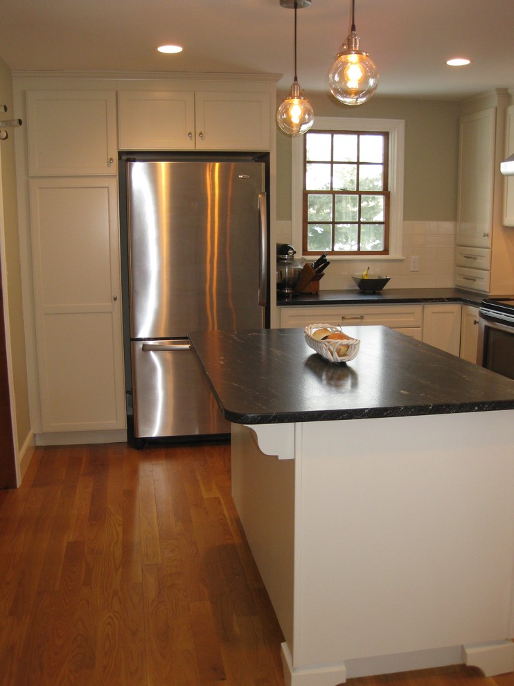 Transitional l-shaped medium tone wood floor eat-in kitchen photo in Boston with an undermount sink, shaker cabinets, white cabinets, quartz countertops, white backsplash, ceramic backsplash, stainless steel appliances, an island and black countertops