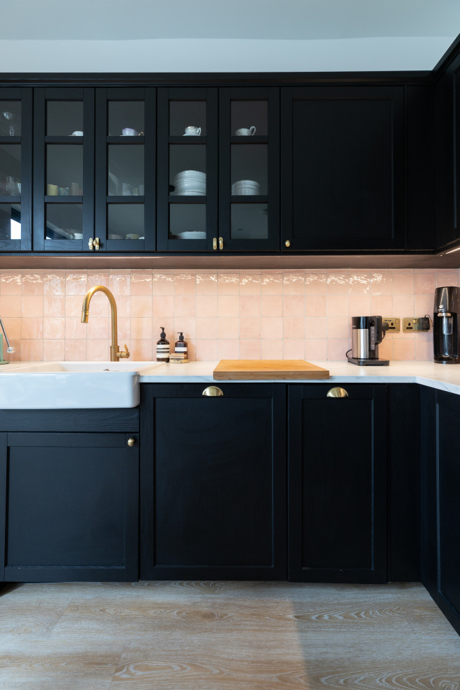 Large contemporary l-shaped separate kitchen in London with a farmhouse sink, black cabinets, pink splashback, ceramic splashback, black appliances, light hardwood floors and beige floor.