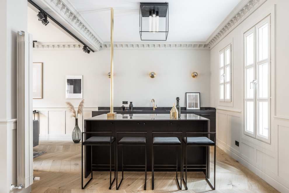 This is an example of a scandinavian galley seated home bar in Madrid with an undermount sink, flat-panel cabinets, black cabinets, light hardwood floors, beige floor and black benchtop.
