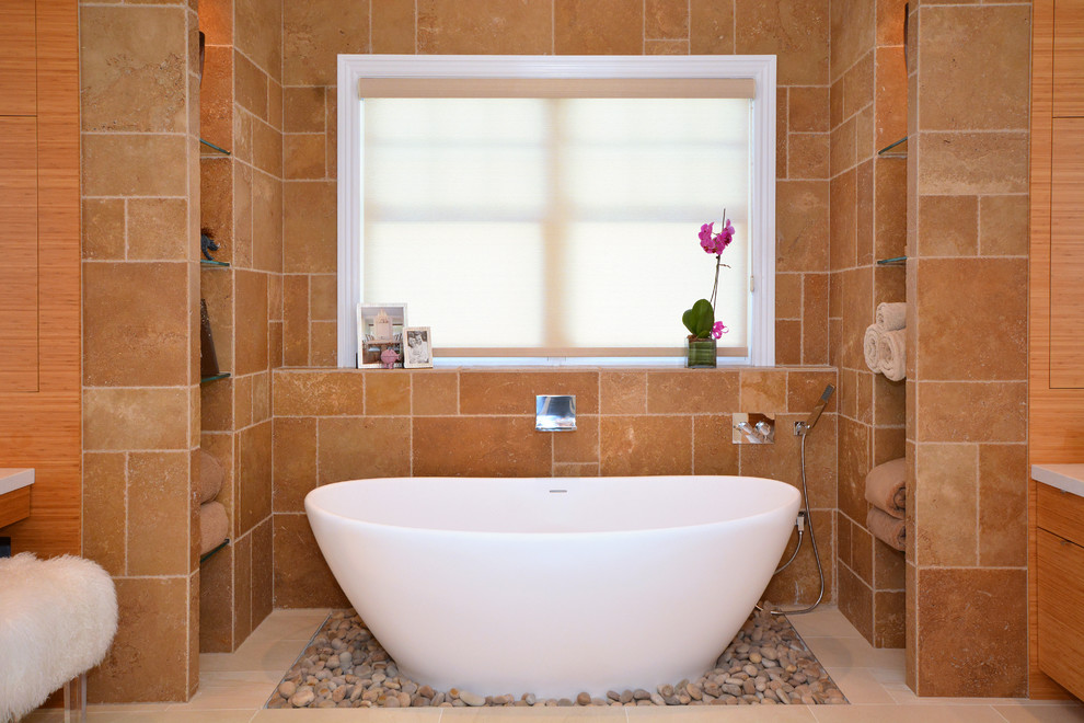 Photo of a large transitional master bathroom in New York with a freestanding tub, flat-panel cabinets, medium wood cabinets, an alcove shower, a one-piece toilet, beige tile, travertine, beige walls, porcelain floors, a vessel sink, glass benchtops, beige floor and a hinged shower door.