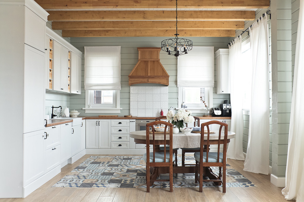 Country l-shaped eat-in kitchen in Moscow with a farmhouse sink, shaker cabinets, white cabinets, wood benchtops, white splashback, light hardwood floors and no island.