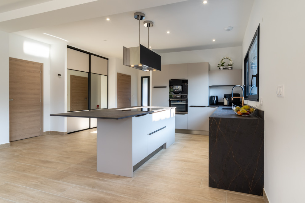 Mid-sized contemporary l-shaped open plan kitchen in Lyon with an integrated sink, beaded inset cabinets, beige cabinets, tile benchtops, black splashback, ceramic splashback, panelled appliances, light hardwood floors, with island, brown floor and black benchtop.