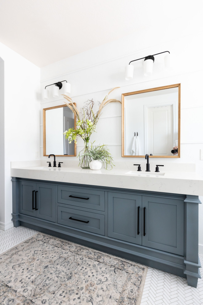 Modelo de cuarto de baño principal, doble y de pie clásico renovado con armarios estilo shaker, puertas de armario azules, bañera exenta, encimera de cuarzo compacto y suelo blanco