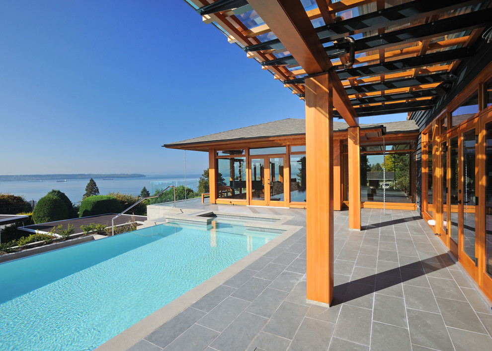 This is an example of a large contemporary backyard rectangular infinity pool in Vancouver with tile.